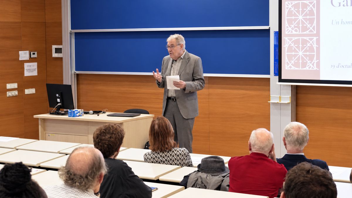 Manuel Castellet addresses the audience, with the title slide of the gallery inauguration on the screen.