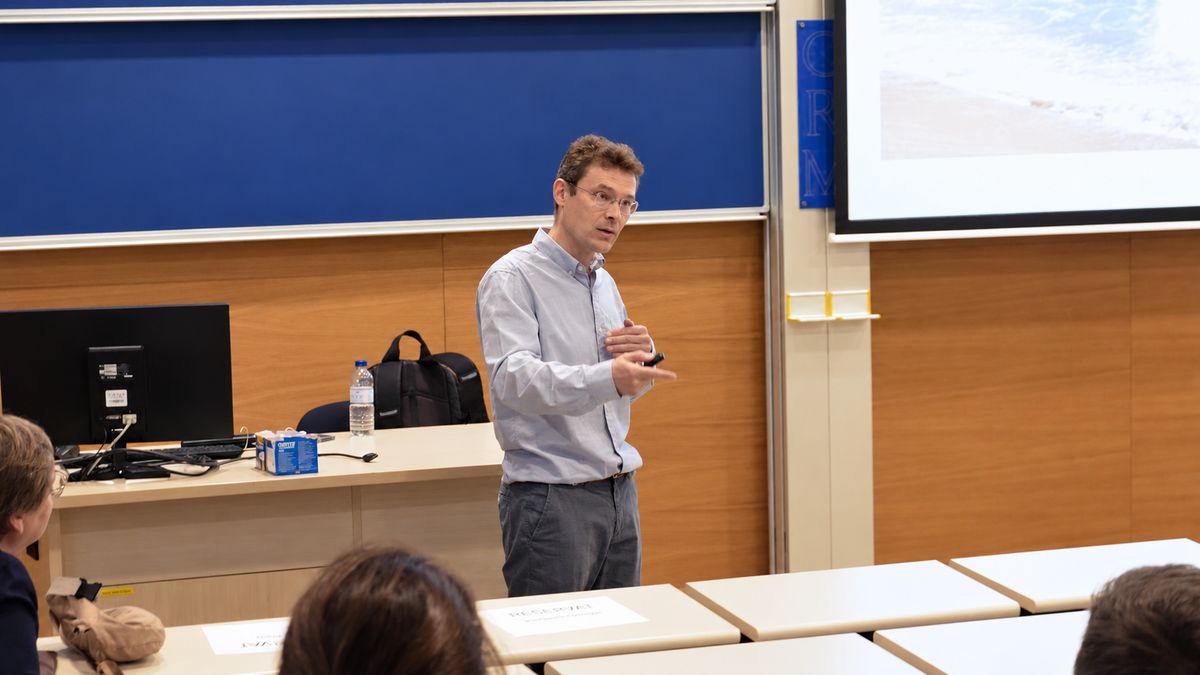 Sergey Tikhonov speaks in front of the lecture hall’s blackboards, beside a slide showing the sea.
