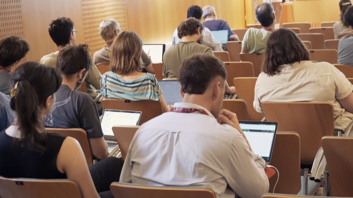 Workshop participants, seen from behind, following a talk with their laptops open