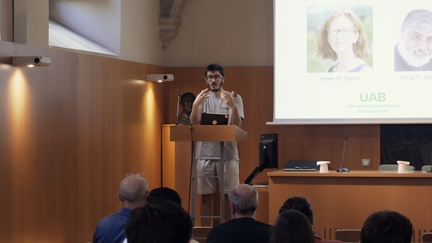 Juan Arellano-Tintó at the lectern in front of a slide with photographs of two researchers and the logo of the Universitat Autònoma de Barcelona